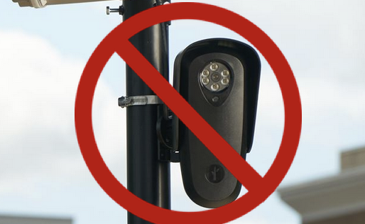 A Flock surveillance camera on a light pole, with a big red circle and slash on top.